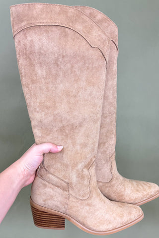 Beige knee-high boot held by a hand against a gray background