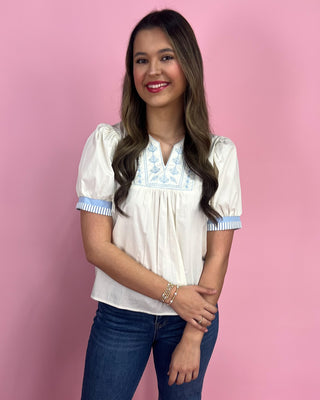 Woman wearing a white blouse with blue accents against a pink background