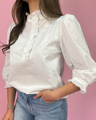 White blouse with lace details worn by a person on a pink background