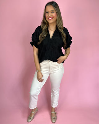 Woman wearing a black top and white pants against a pink background