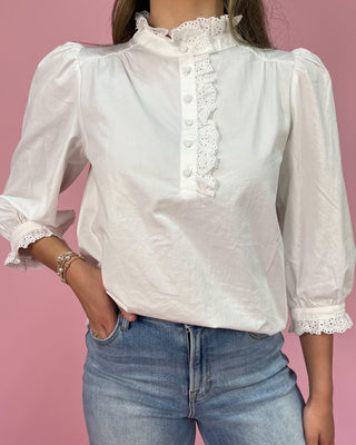 White blouse with lace details and blue jeans against a pink background