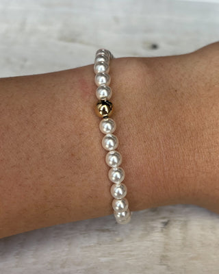 Pearl bracelet with a gold accent on a wrist against a neutral background