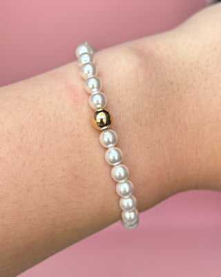 Pearl bracelet with a gold accent on a wrist against a pink background