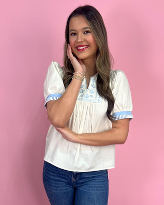 Woman wearing a white blouse with blue accents against a pink background