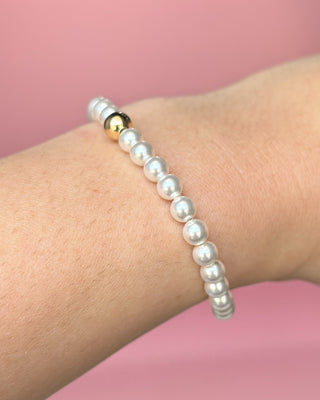 Pearl bracelet with a gold accent on a wrist against a pink background