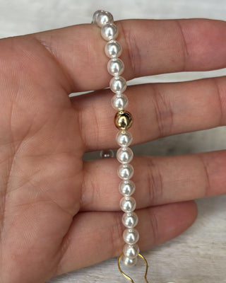 Pearl bracelet with a gold clasp held in a hand against a neutral background