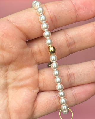 Pearl bracelet with a gold bead held in a hand against a pink background