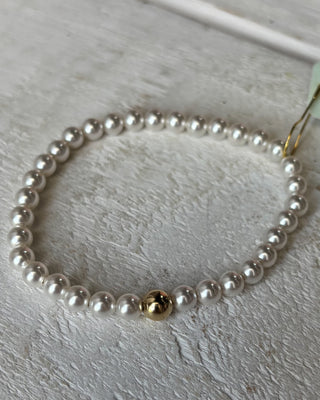 Pearl necklace with a gold bead on a light wooden surface