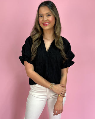Woman wearing a black blouse and white pants against a pink background