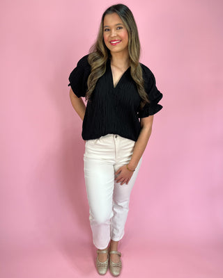 Woman wearing a black top and white pants against a pink background