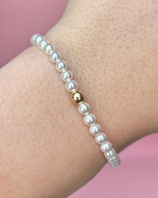 Pearl bracelet with a gold bead on a wrist against a pink background