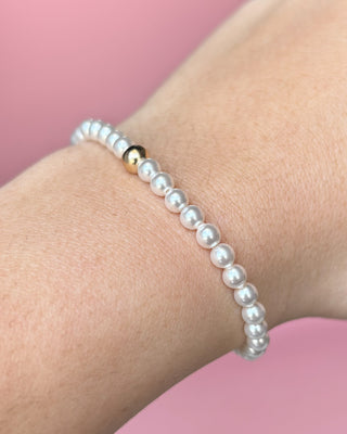 Pearl bracelet on a wrist with a pink background