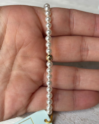 Pearl bracelet with a gold bead held between fingers