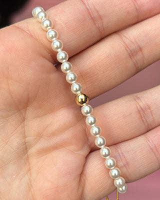 Pearl bracelet with a gold clasp held in a hand against a pink background