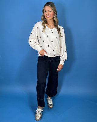 Cream polka dot textured V-neck top with contrasting brown dots, relaxed drop shoulders, long sleeves
