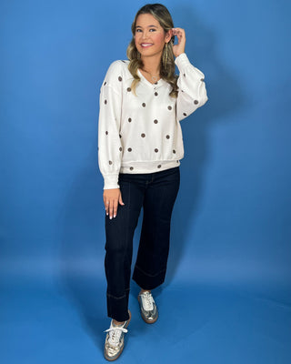 Cream polka dot textured V-neck top with contrasting brown dots, relaxed drop shoulders, long sleeves