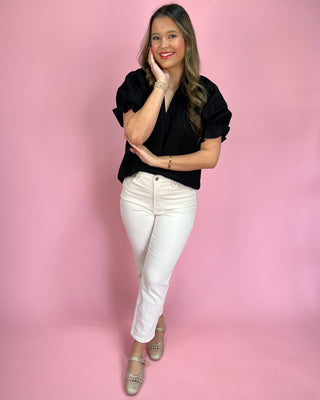 Woman wearing a black top and white pants against a pink background
