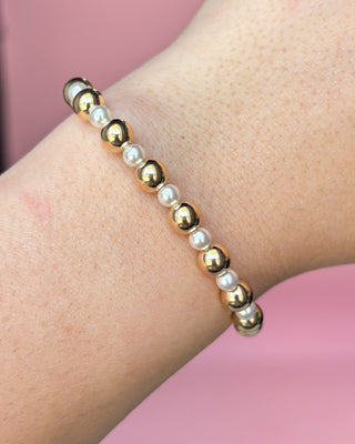 Bracelet with gold and pearl beads on a wrist against a pink background