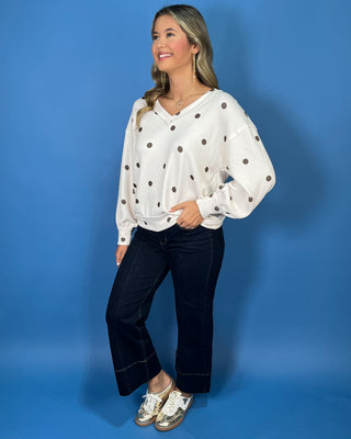 Cream polka dot textured V-neck top with contrasting brown dots, relaxed drop shoulders, long sleeves