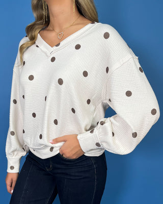 Cream polka dot textured V-neck top with contrasting brown dots, relaxed drop shoulders, long sleeves