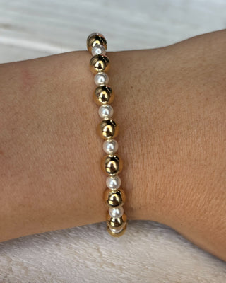 Gold and pearl beaded bracelet on a wrist against a neutral background