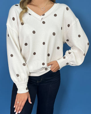 Cream polka dot textured V-neck top with contrasting brown dots, relaxed drop shoulders, long sleeves
