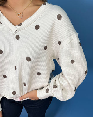 Cream polka dot textured V-neck top with contrasting brown dots, relaxed drop shoulders, long sleeves