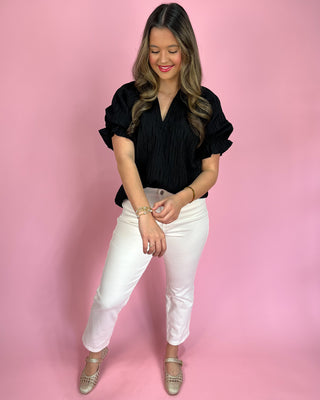 Woman wearing a black top and white pants against a pink background