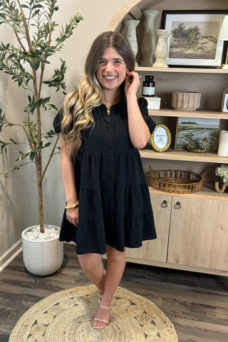 Woman in a black dress standing in a room with decor elements.