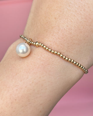 Gold bracelet with a pearl on a wrist against a pink background