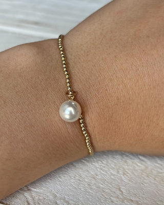 Gold bracelet with a pearl on a wrist against a neutral background