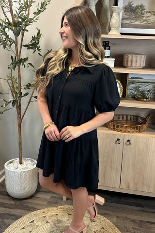 Woman in a black dress standing in a room with decor elements.