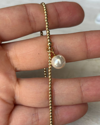 Gold bracelet with a pearl on a hand against a white background