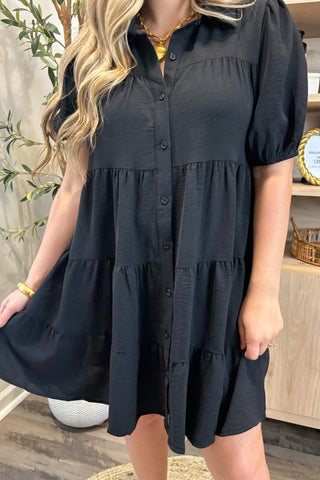 Woman wearing a black tiered dress indoors with a blurred background