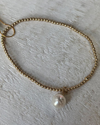 Gold beaded bracelet with a pearl charm on a light wooden surface