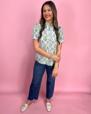 Woman wearing a floral blouse and jeans against a pink background