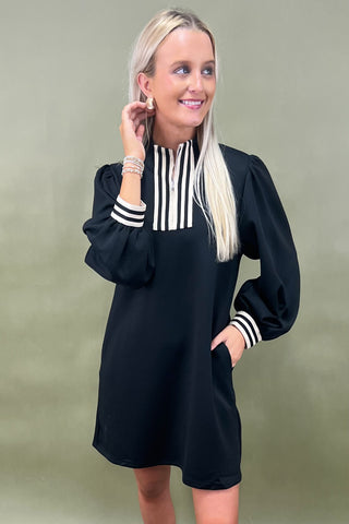 Woman wearing a black dress with white striped details against a green background