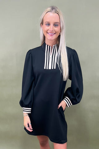 Woman wearing a black dress with white stripe details against a green background