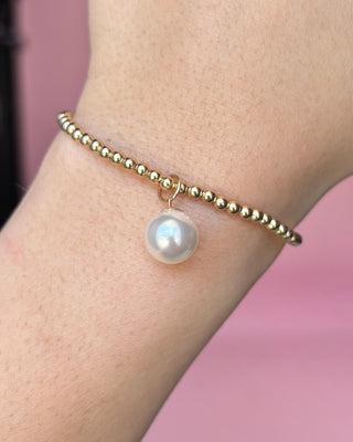Gold bracelet with a pearl on a wrist against a pink background