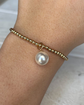 Gold bracelet with a pearl charm on a wrist against a neutral background