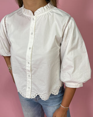 White blouse with lace details worn by a person on a pink background