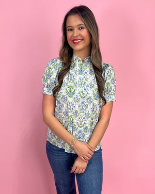 Woman wearing a floral blouse and jeans against a pink background