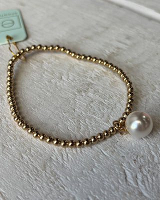 Gold beaded bracelet with a pearl on a light gray surface