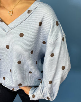 Light blue textured polka dot V-neck top with contrasting brown dots, relaxed drop shoulders, long sleeves