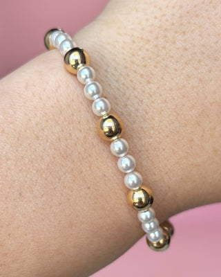 Bracelet with gold and white beads on a wrist against a pink background