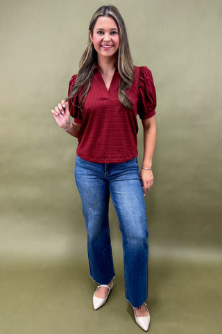 Woman wearing a red blouse and blue jeans against a green background