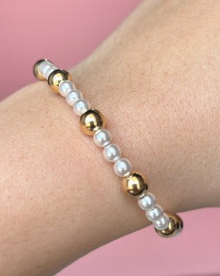 Bracelet with pearls and gold beads on a wrist against a pink background