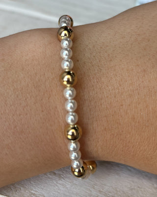 Pearl and gold beaded bracelet on a wrist against a neutral background