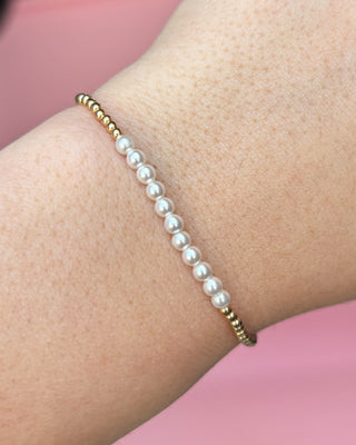 Pearl bracelet with gold beads on a wrist against a pink background