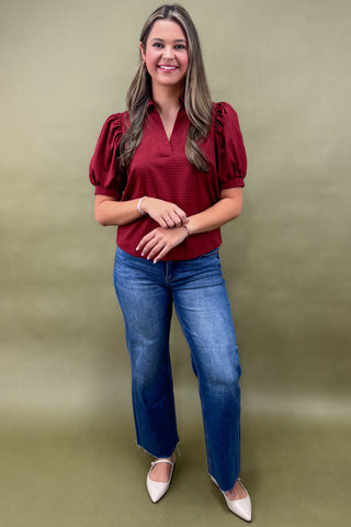 Woman wearing a red blouse and blue jeans against a green background